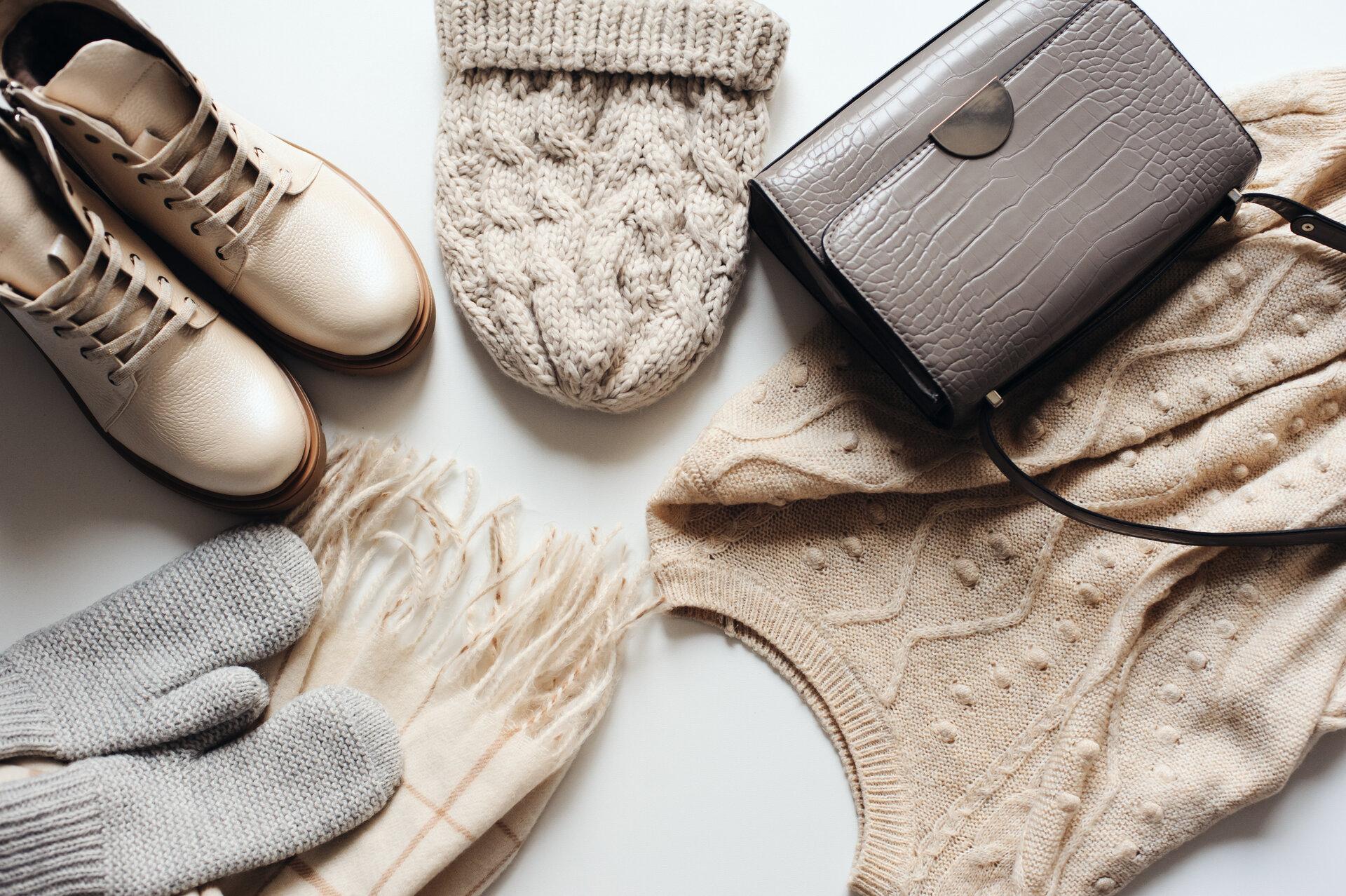 Wintermode-Set von Frauenkleidung in neutralen Tönen: warmer Pullover, Hut, Fäustlinge, Schuhe und Handtasche auf weißem Hintergrund