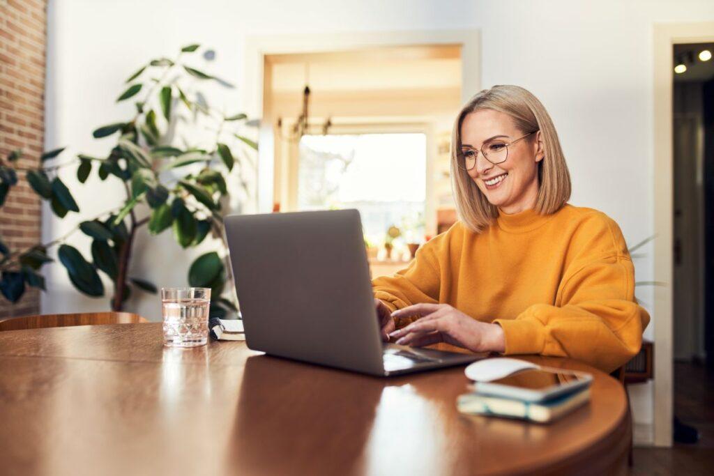 Frau sitzt entspannt am Tisch und arbeitet an Laptop – Ergebnis einer professionellen Macbook Reparatur und guter Pflege