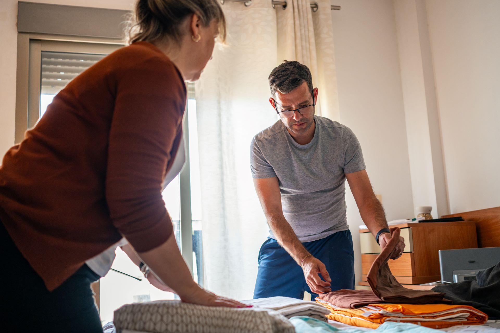Zwei Personen falten gemeinsam Wäsche in einem hellen Schlafzimmer.